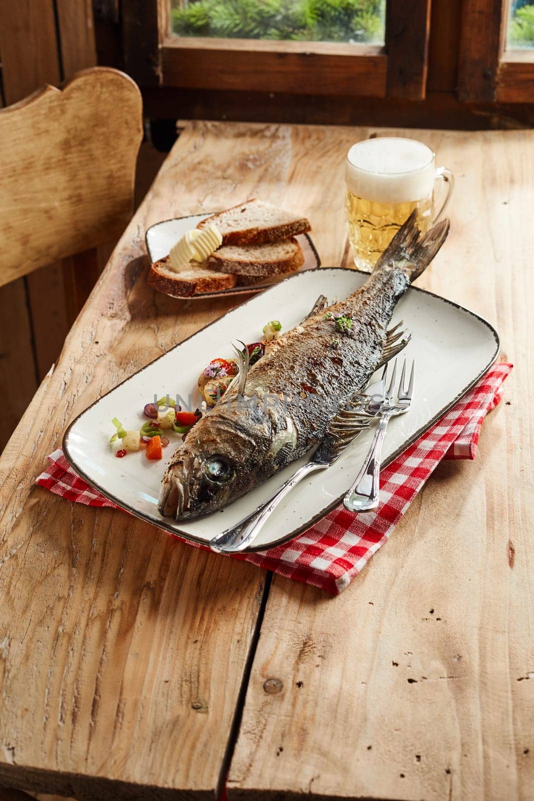 Whole oven roasted sea bass for a pub lunch served with a cold frothy beer and sliced rye bread with foreground copy space