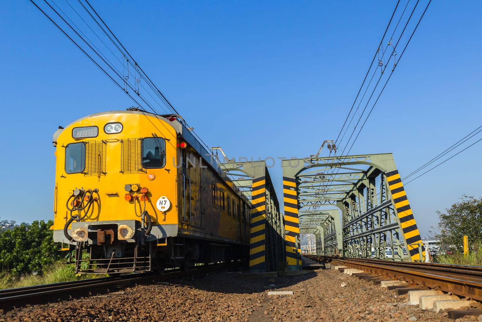 Train passenger coaches closeup on rail tracks crossing bridge to city countryside.