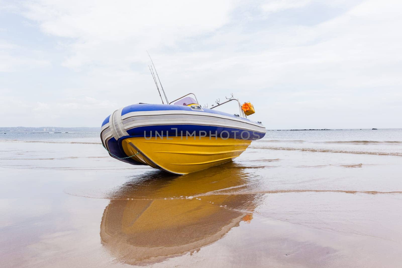 Fishing inflatable boat fiber-glass hull outboard motors craft on beach sands at water edge.
