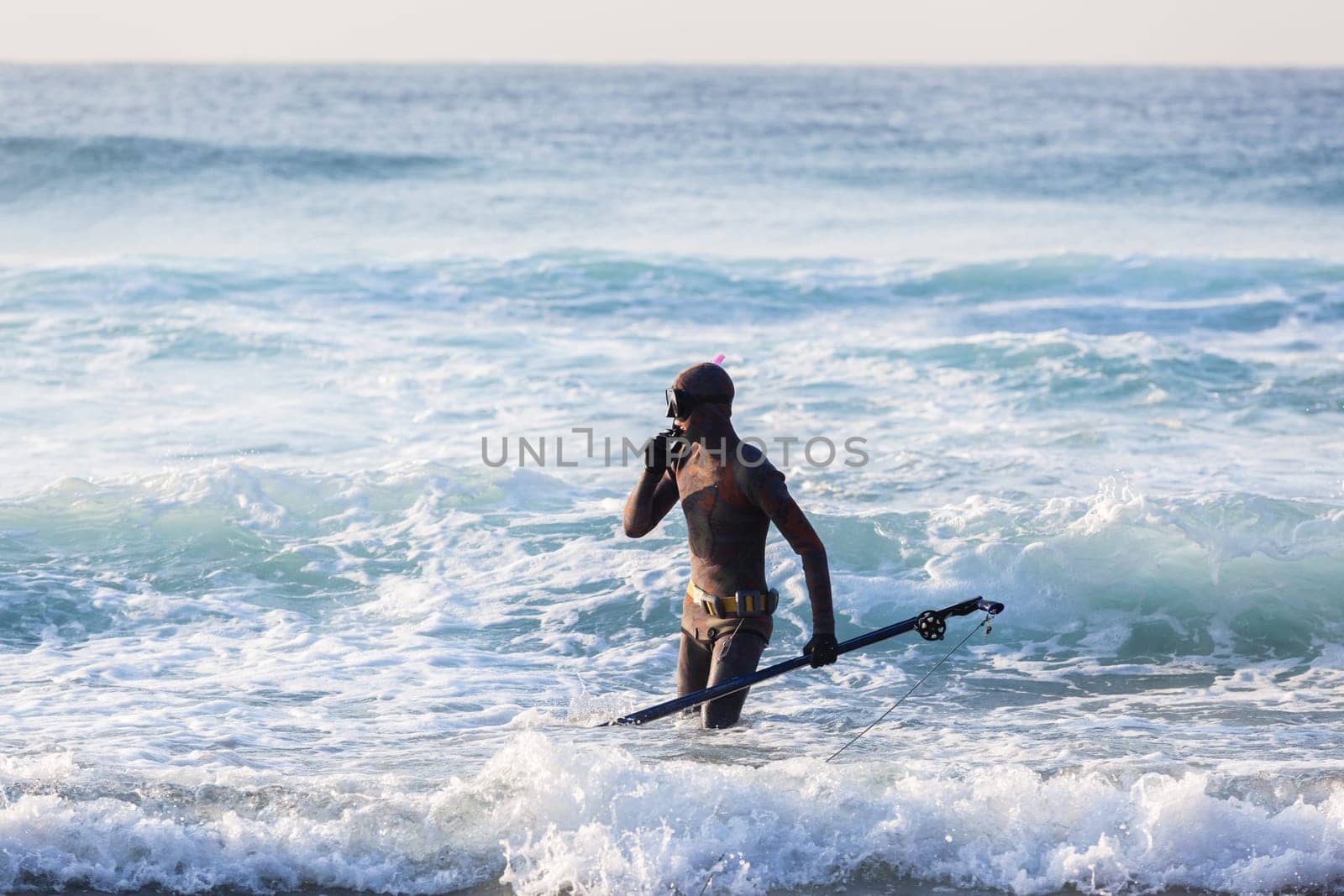 Spearfishing unidentified diver on beach about to enter blue ocean sea waters swimming sporting lifestyle