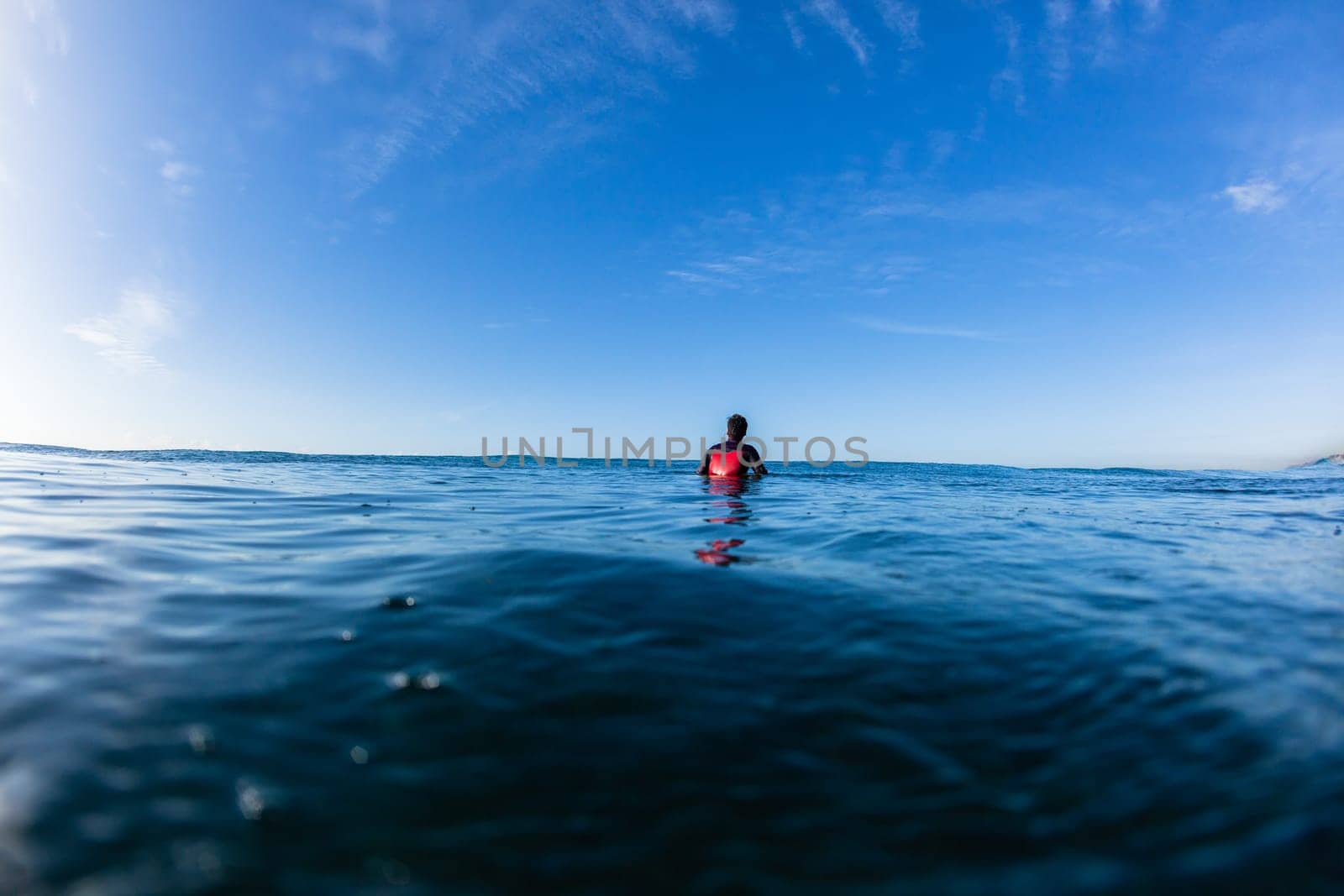 Surfer surfing sitting waiting ocean waves on blue horizon water photo.