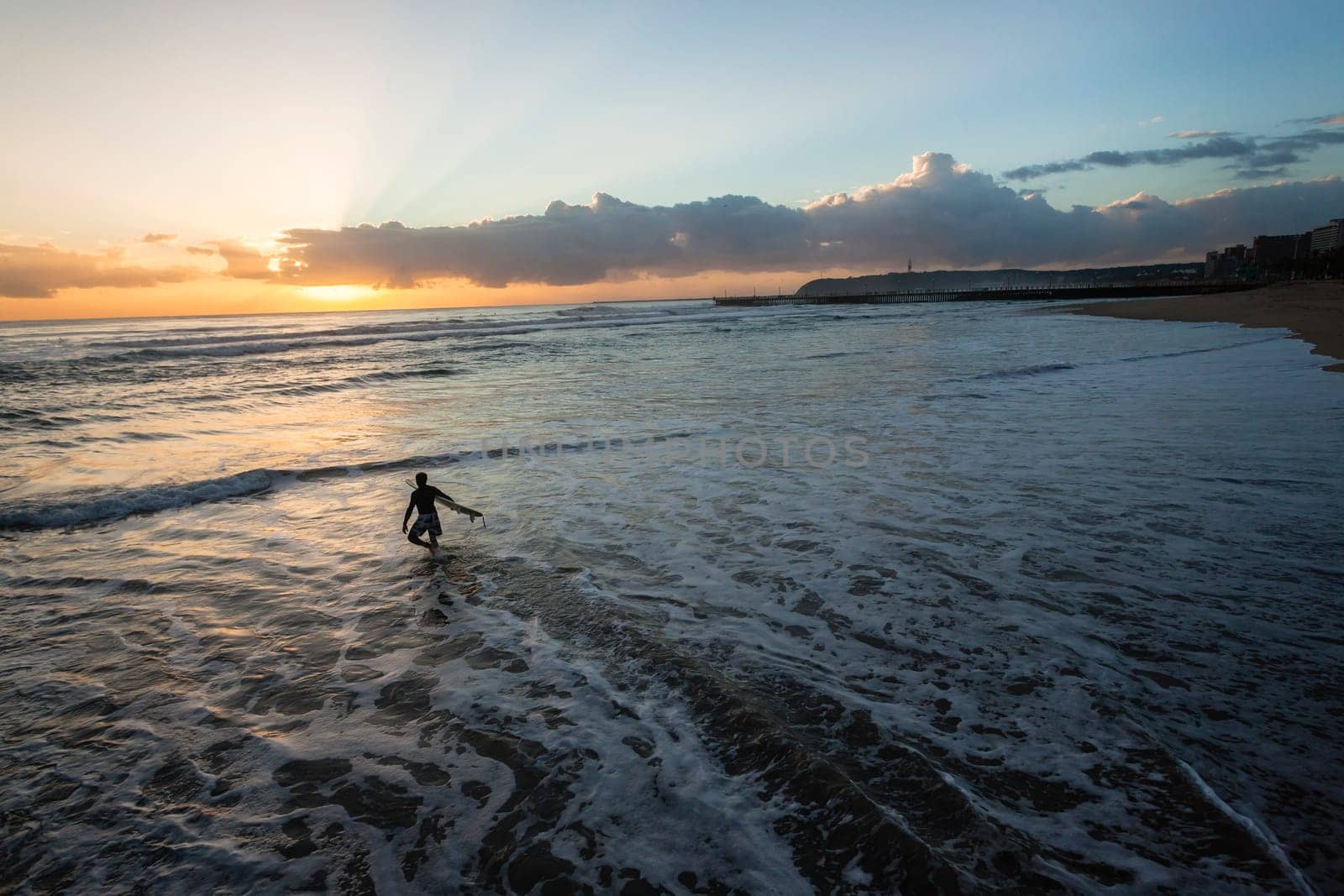 Surfer silhouetted dawn sunrise going surfing beach entry into ocean wave landscape.