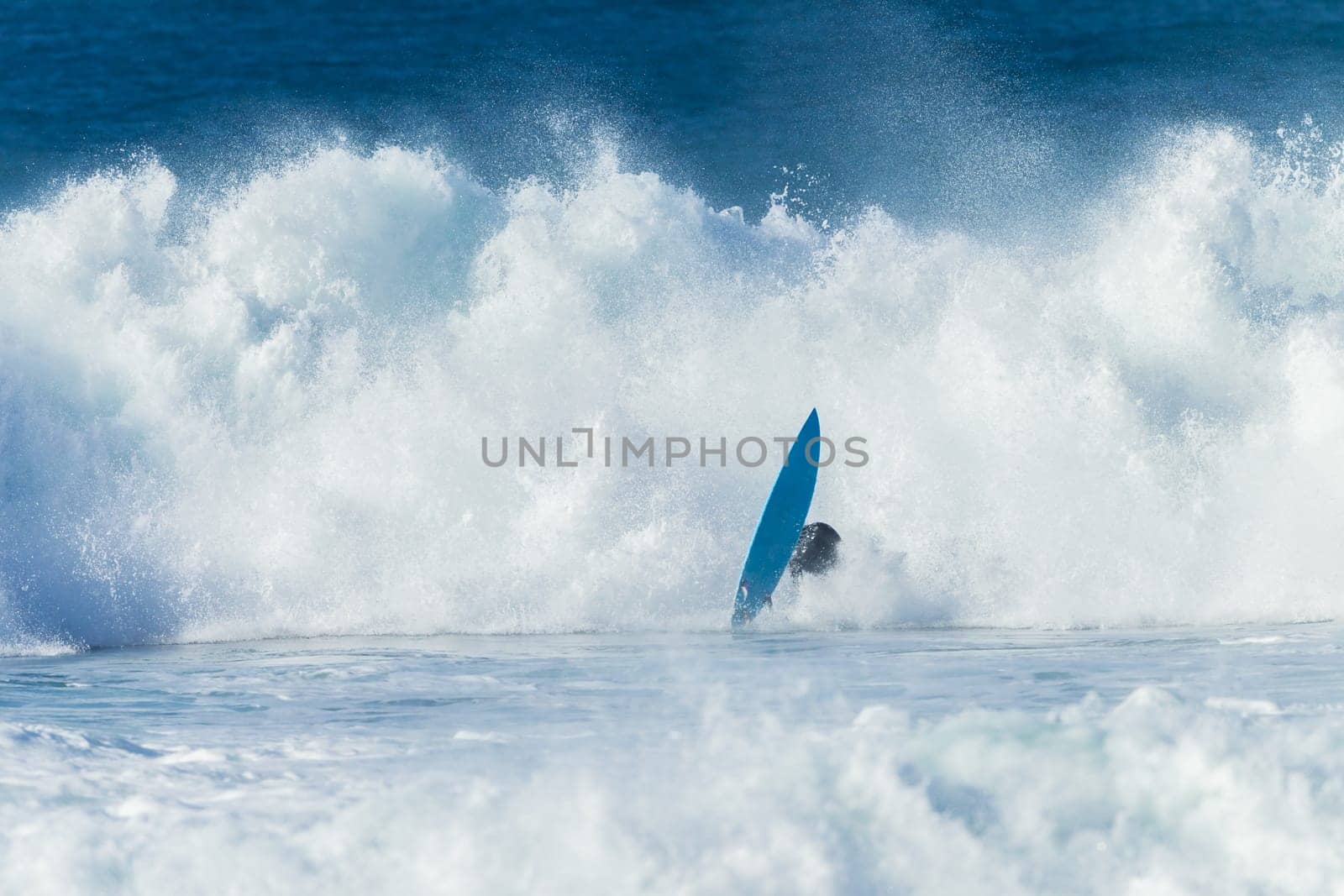 Surfing surfer crashing wipe-out large ocean wave with surfboard flying front of white water.