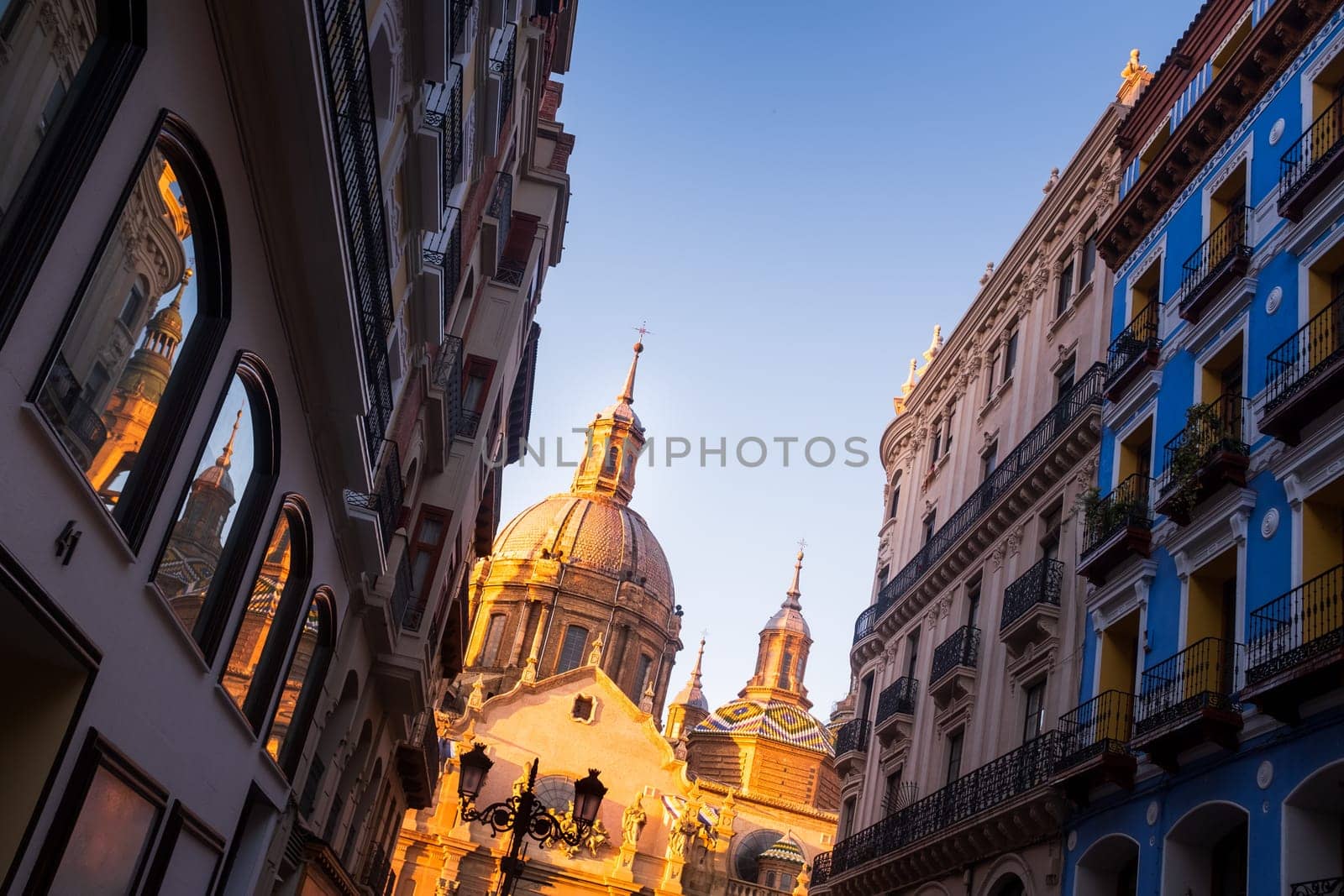 Basilica Of Our Lady Of The Pilar and historical buildings as seen from below, Zaragoza from street level, reflection of Cathedral details in glass windows on the left