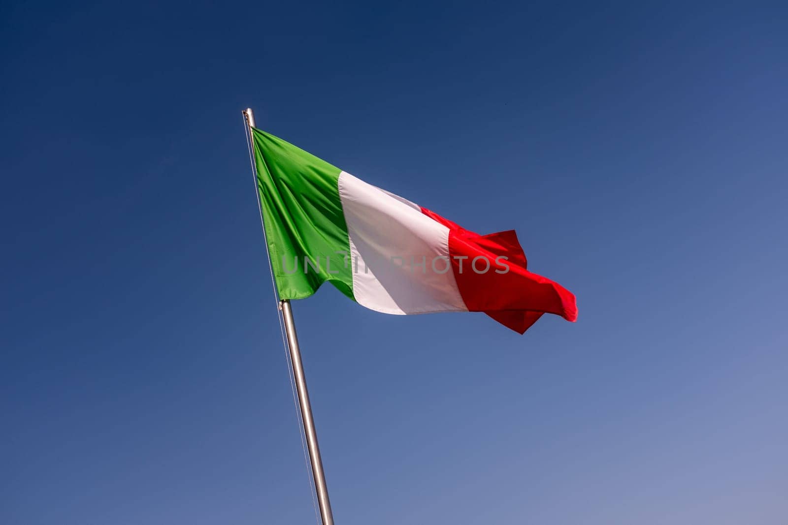 Low angle view of Italy flag waving against the clear blue sky, flagpole tilted to the left