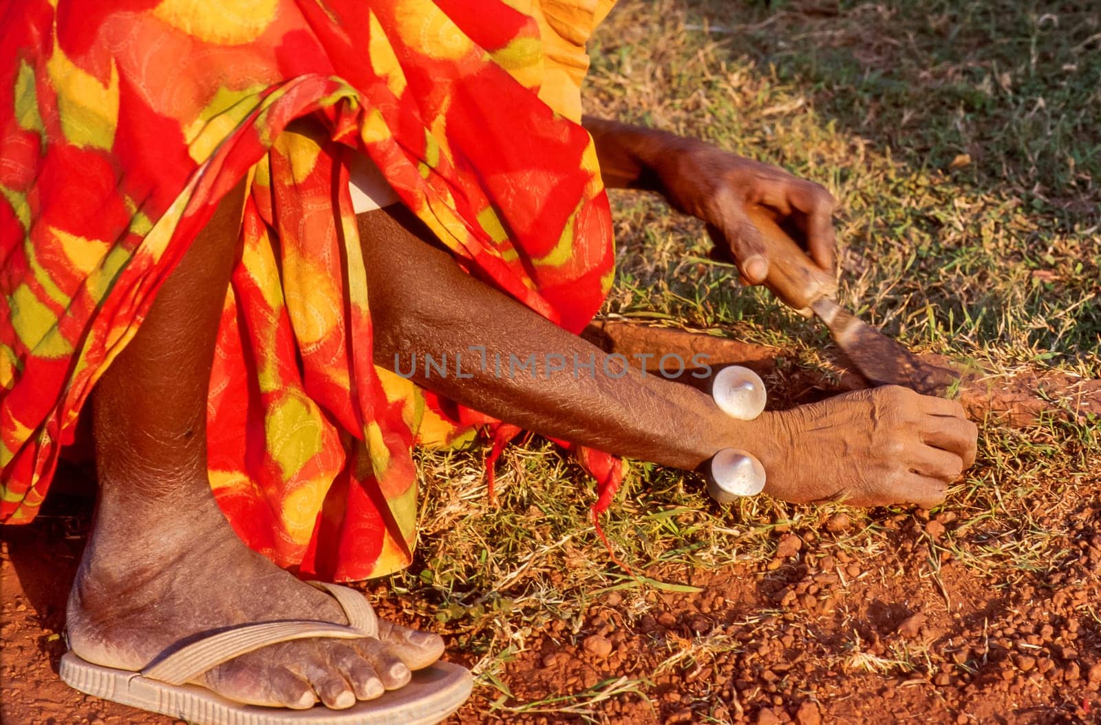 Old woman crouching beside a flowerbed and removing the growing grass on a garden path using her hands