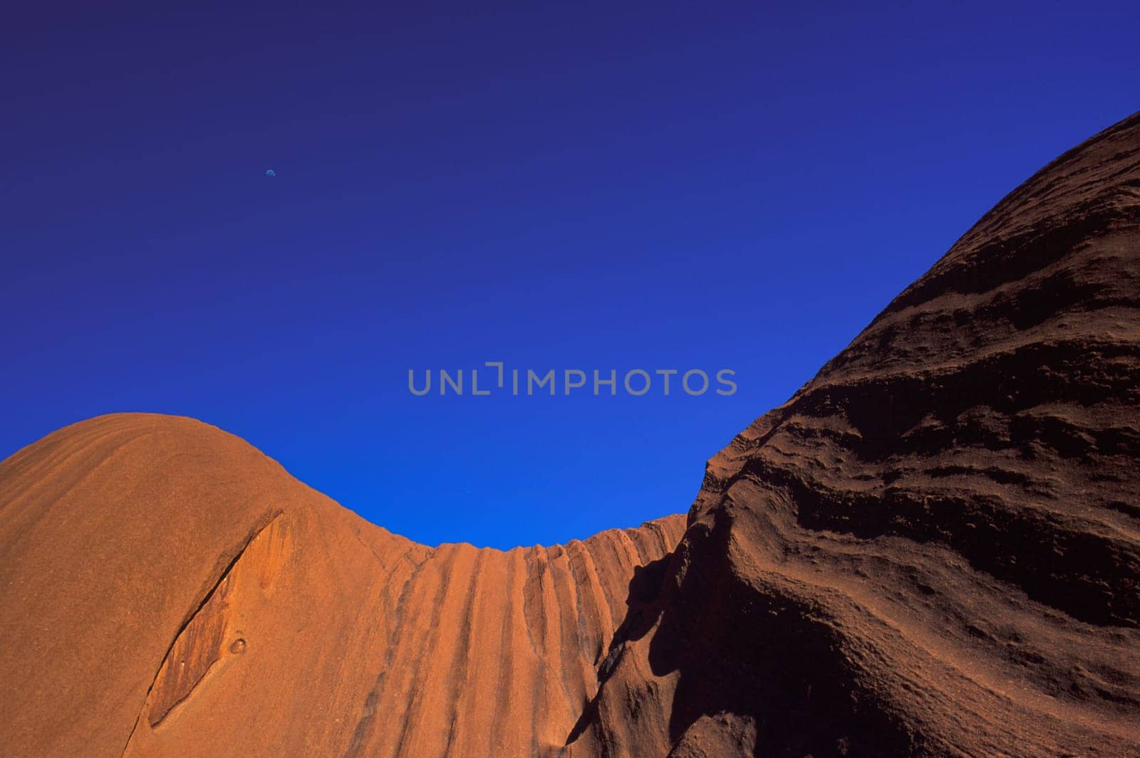 Low angle view of the striations on the surface southern of Uluru, rocks against clear blue sky, the moon in the background, Uluru Kata Tjuta National Park , Australia