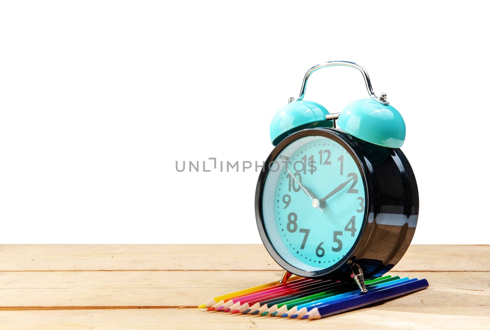 Alarm clock and colored pencils on wooden table isolated over white background. Back to School concept