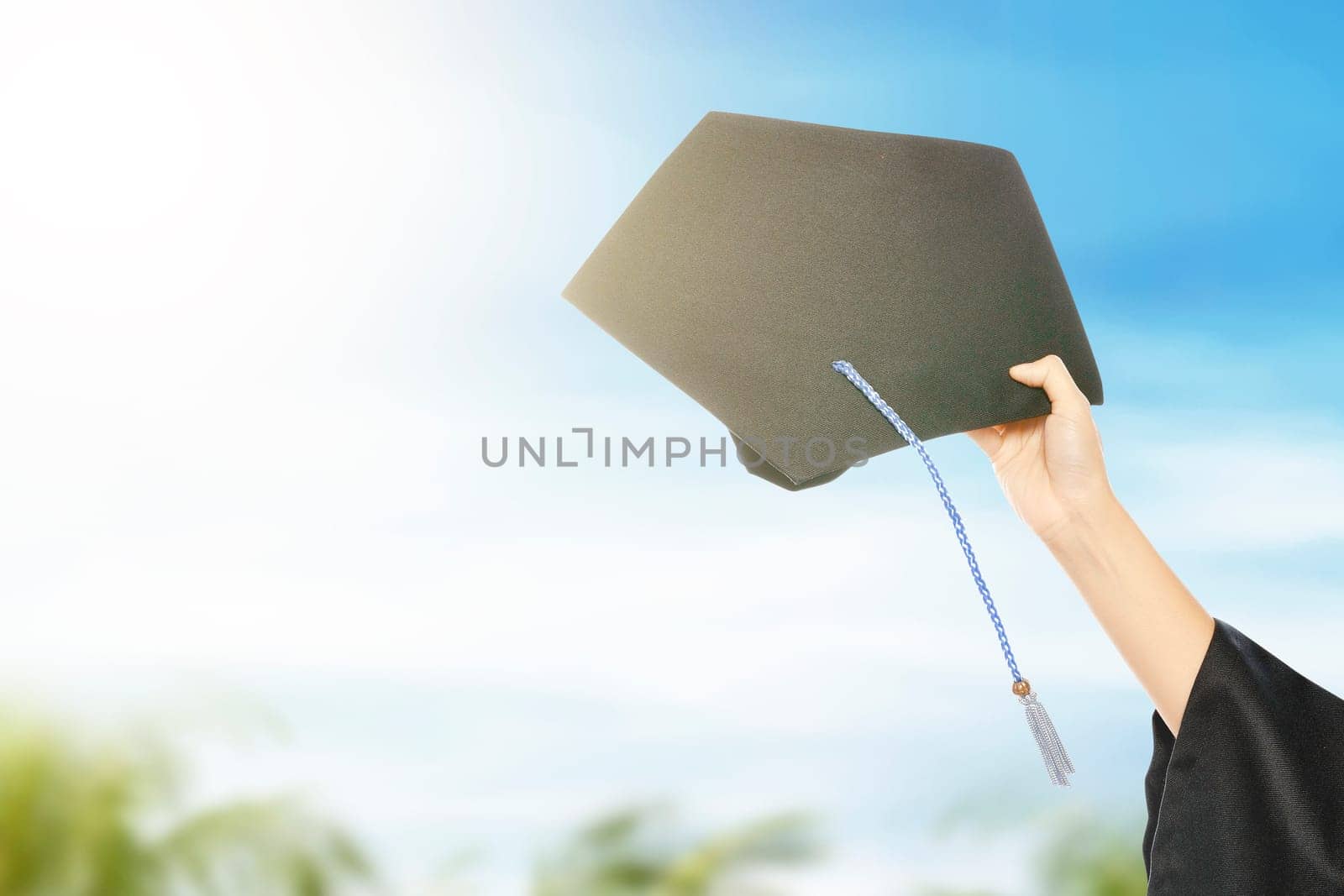 Hand holding graduation hat with blue sky background. Graduation concept