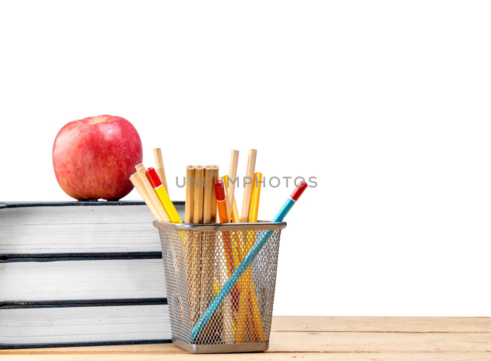 Pile of books with apple and pencils in basket container on wooden table isolated over white background. Back to School concept