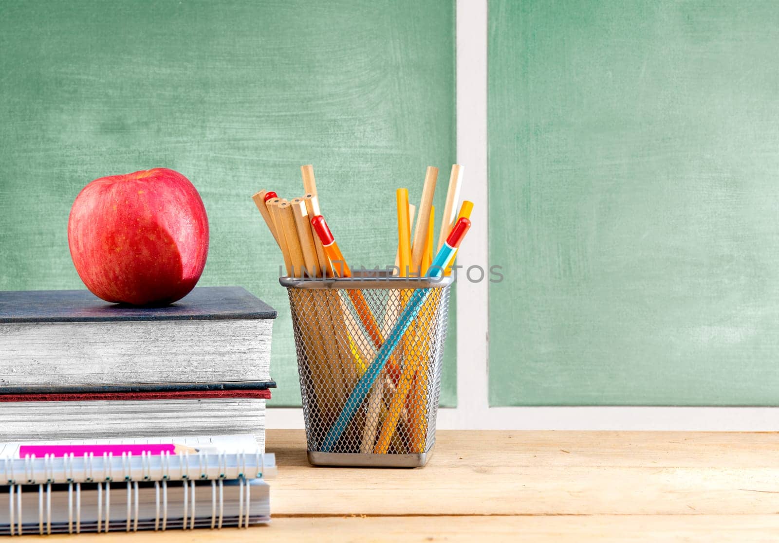 Pile of books with apple and pencils in basket container on wooden table with chalkboard background. Back to School concept