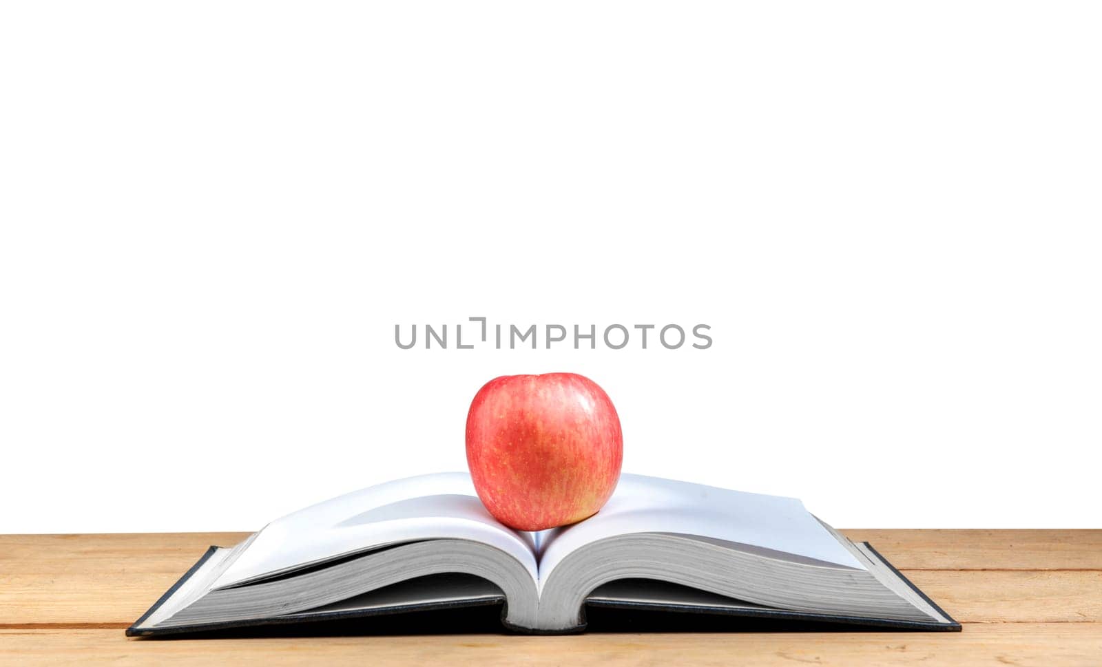 Apple on the middle of opened book on wooden table isolated over white background. Back to School concept