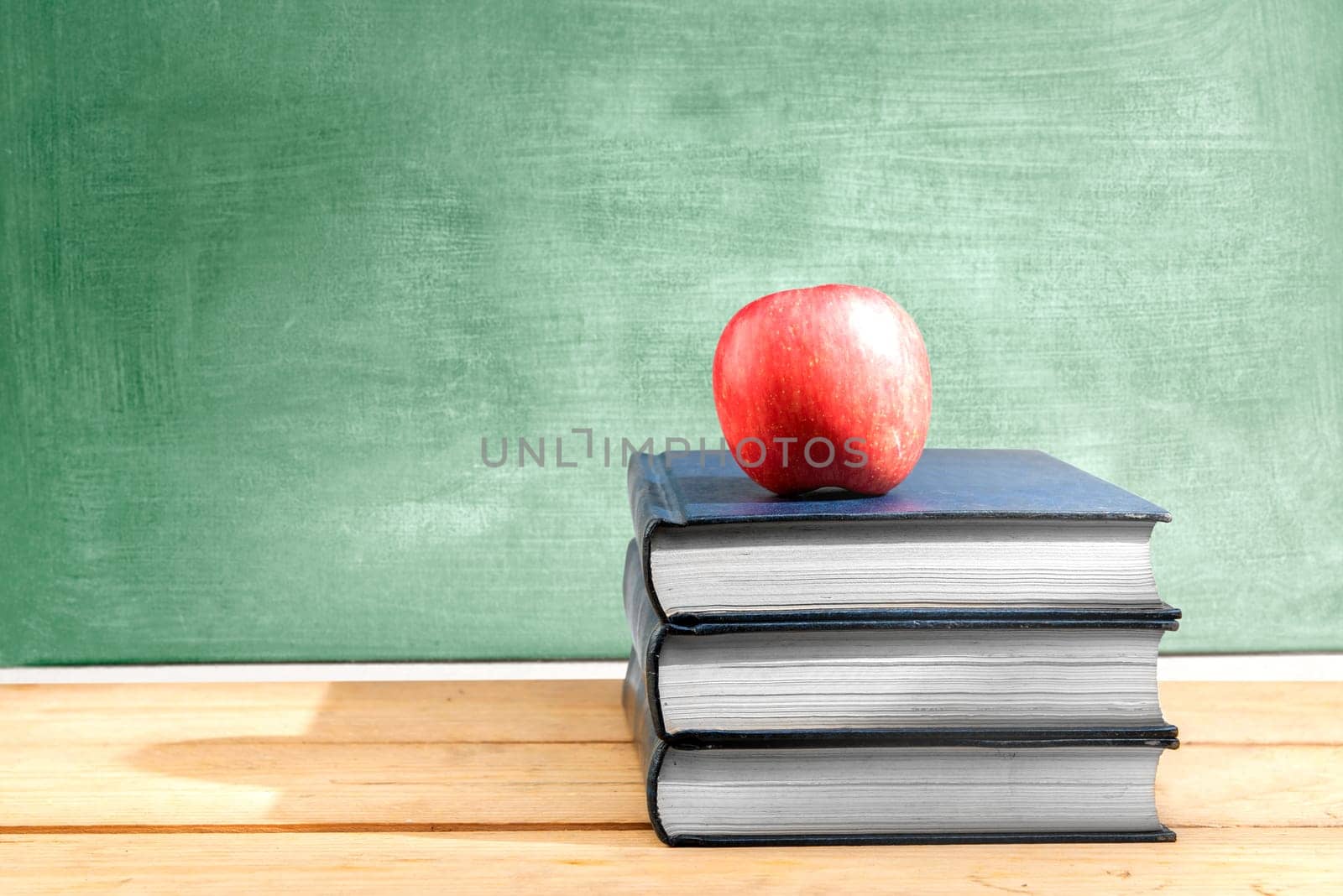 Pile of books with apple on the wooden table with chalkboard background. Back to School concept