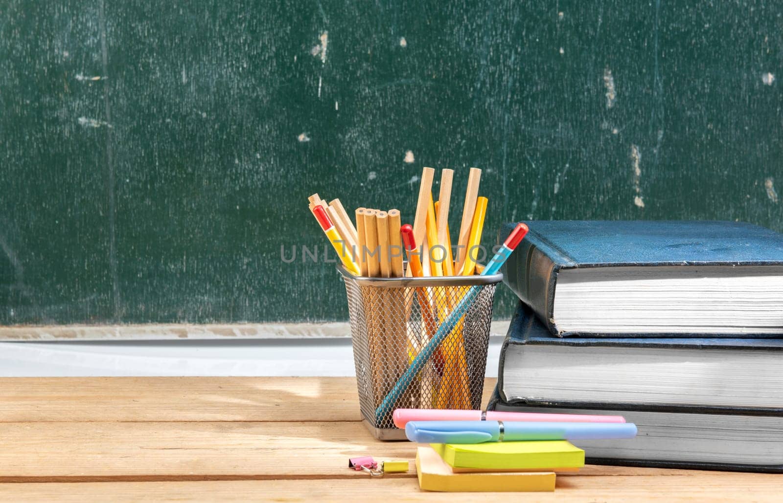 Pile of books with notes paper and pen with pencils in basket container on wooden table with chalkboard background. Back to School concept