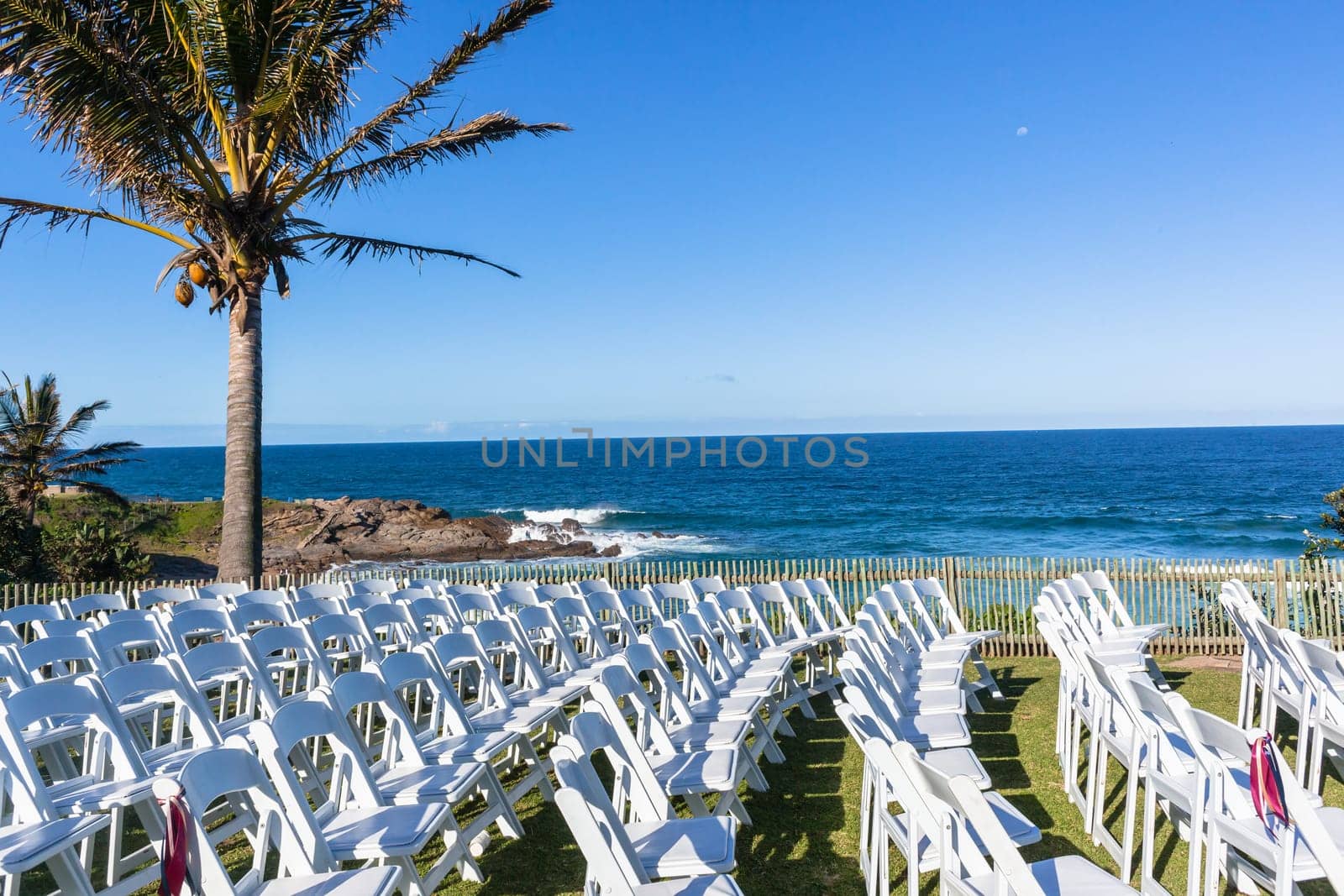 White Chairs dozens setting for Wedding Venue function home lawn front of beach blue ocean horizon summer landscape.