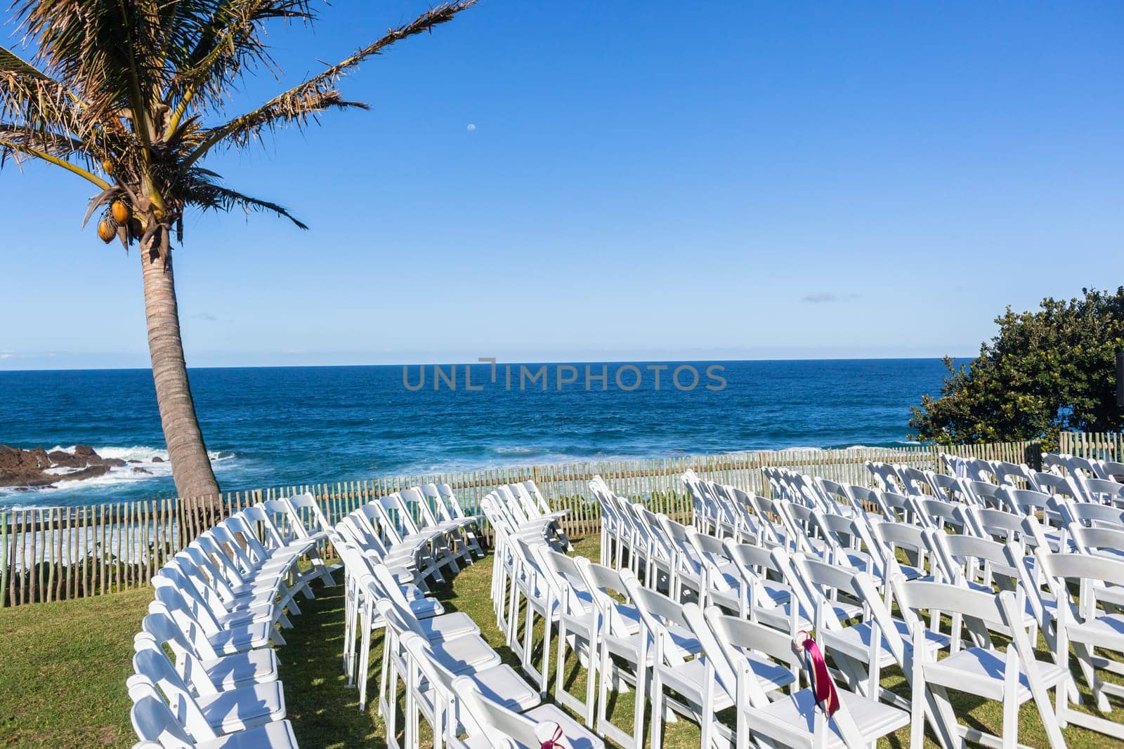 White Chairs dozens setting for Wedding Venue function home lawn front of beach blue ocean horizon summer landscape.