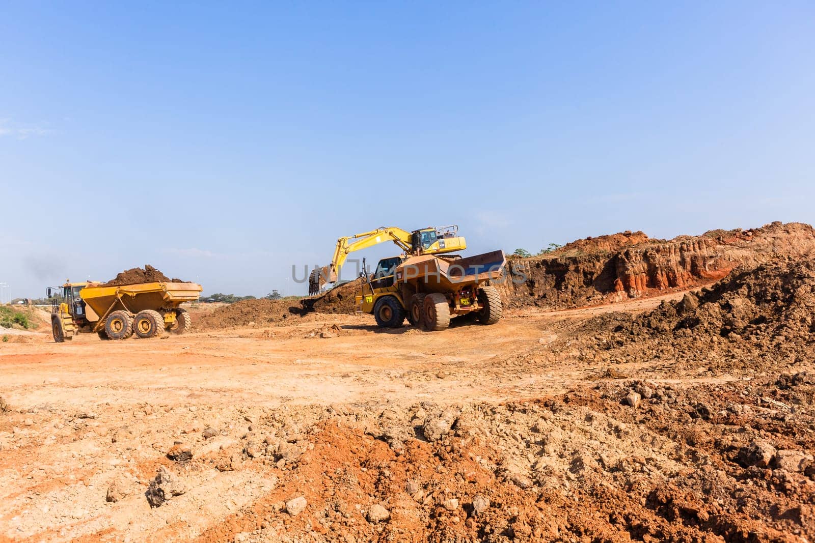 Construction industrial earthworks excavator machine loading earth soil into large truck vehicles.