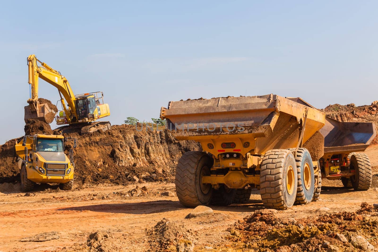 Construction industrial earthworks excavator machine loading earth soil into large truck vehicles.