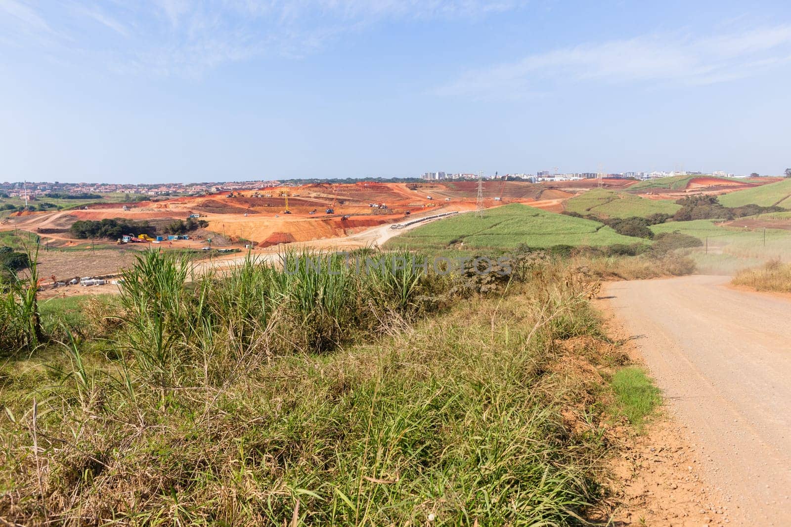 Industrial construction site overlooking large project expansion with graders,excavators,cranes machines into countryside sugarcane fields expanding earthworks infrastructure.