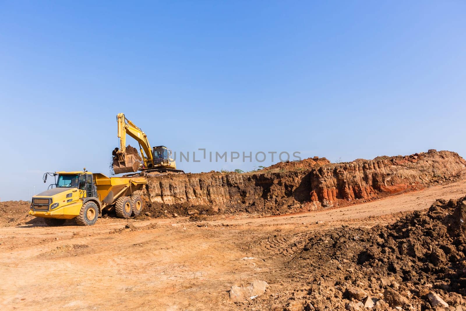 Construction industrial earthworks excavator machine loading earth soil into large truck vehicles.