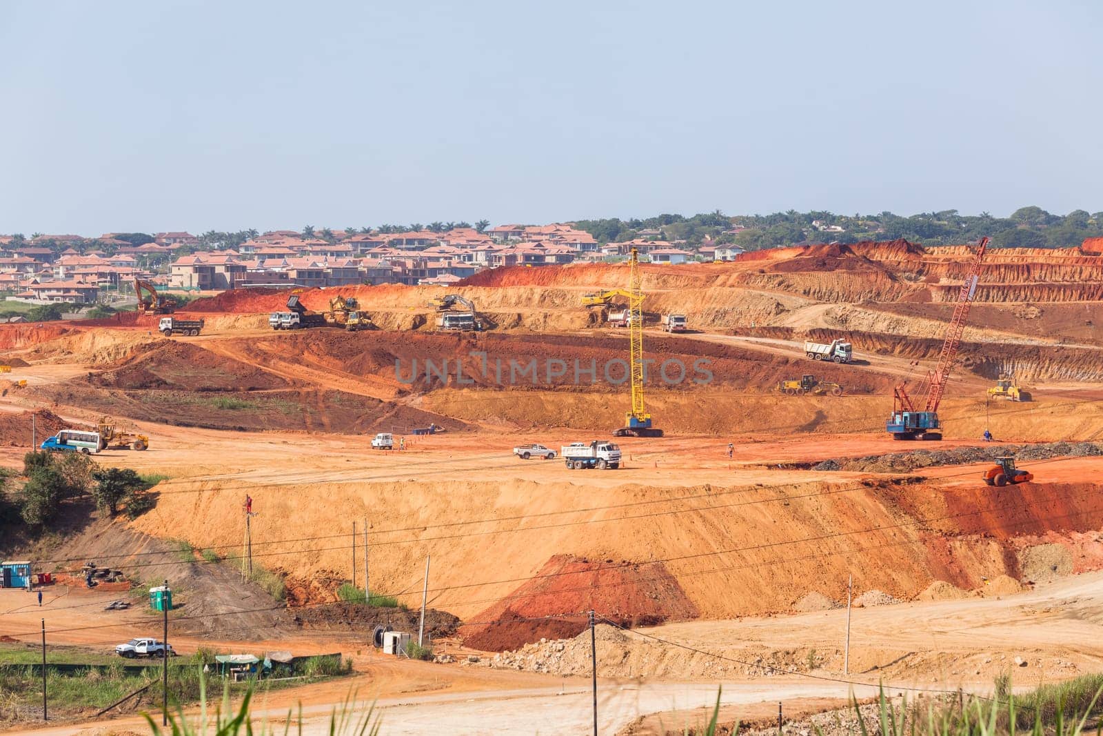 Industrial construction site overlooking large project expansion with graders,excavators,cranes machines into countryside sugarcane fields expanding earthworks infrastructure.