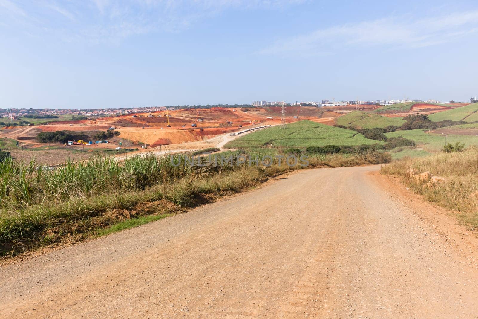 Industrial construction site overlooking large project expansion with graders,excavators,cranes machines into countryside sugarcane fields expanding earthworks infrastructure.