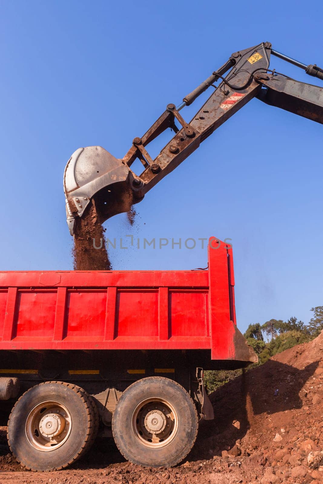 Construction industrial earthworks excavator machine loading earth soil into large truck vehicles.