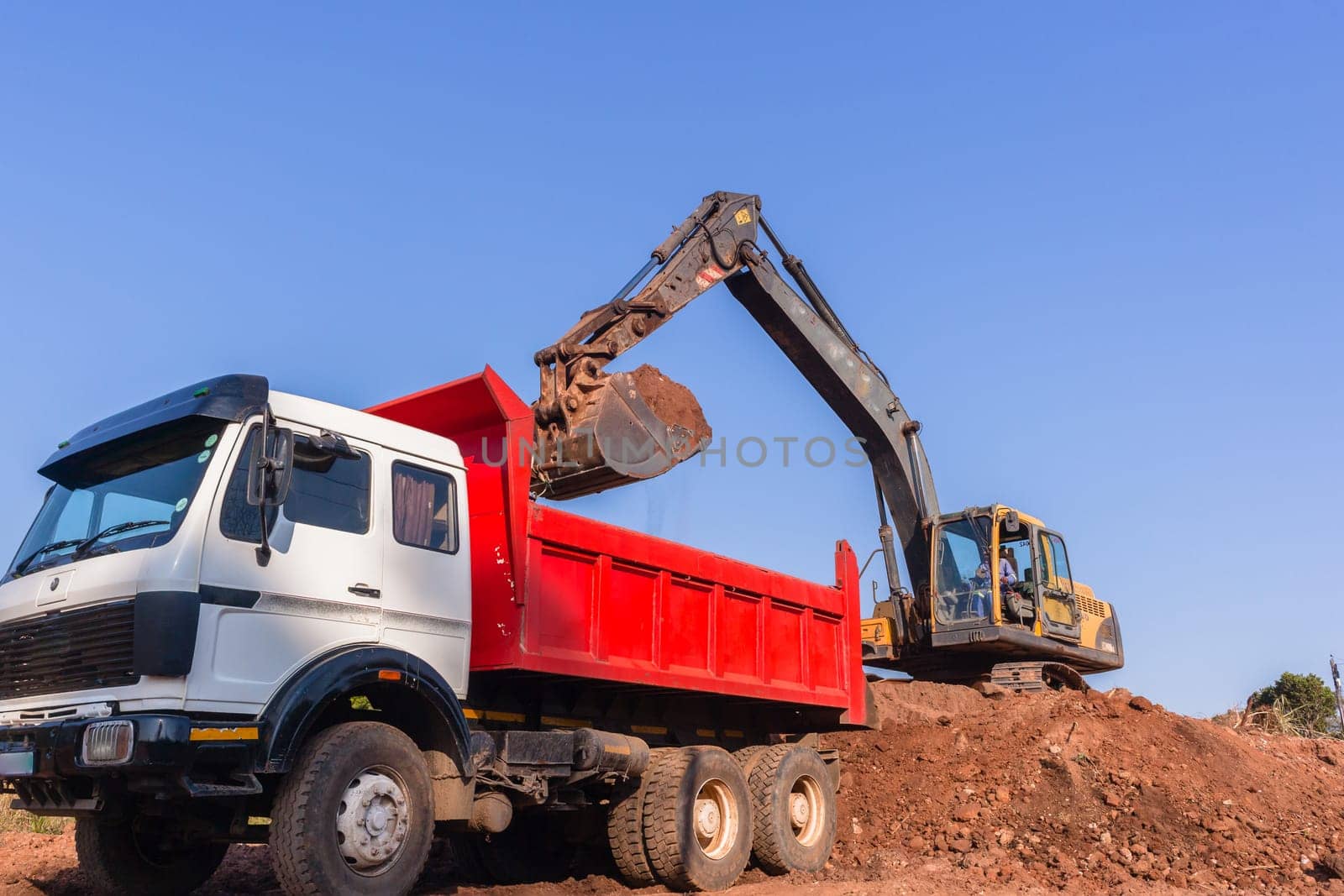 Construction industrial earthworks excavator machine loading earth soil into large truck vehicles.