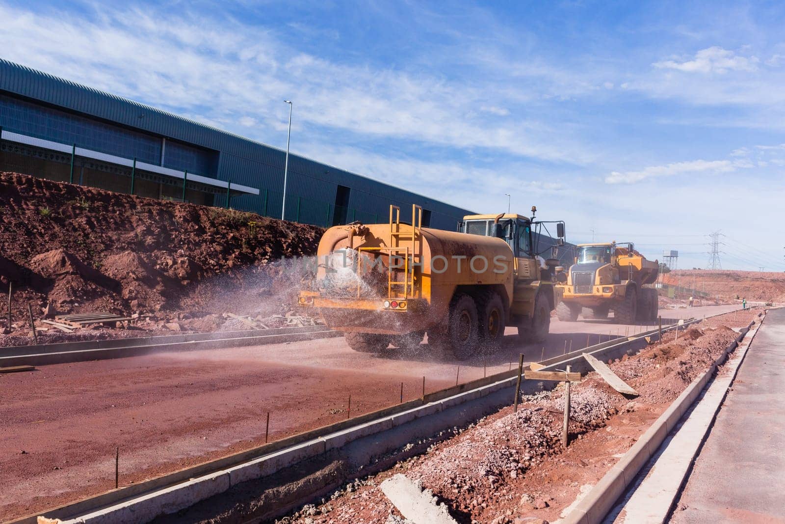 Roadworks construction preparation by industrial vehicles water spraying road surface for asphalt.
