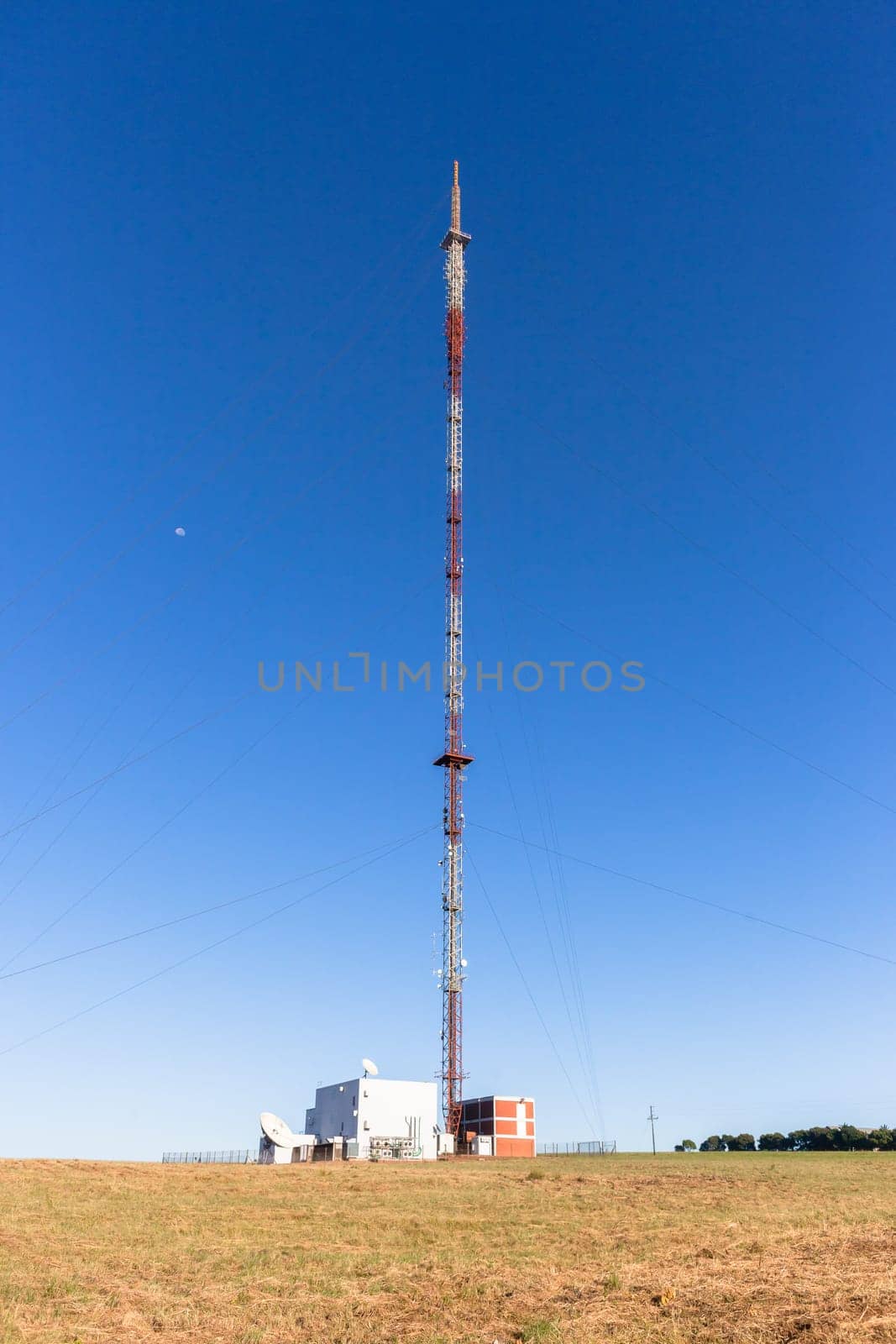 Communications signal tower tall high steel structure,on high ground hilltop for radio tv mobile phones against blue sky.