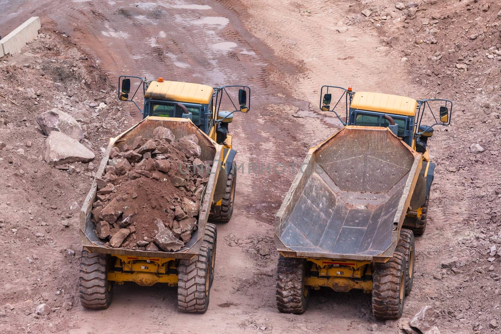 Industrial earthworks loading truck vehicles heavy rocks on construction site overhead photo.