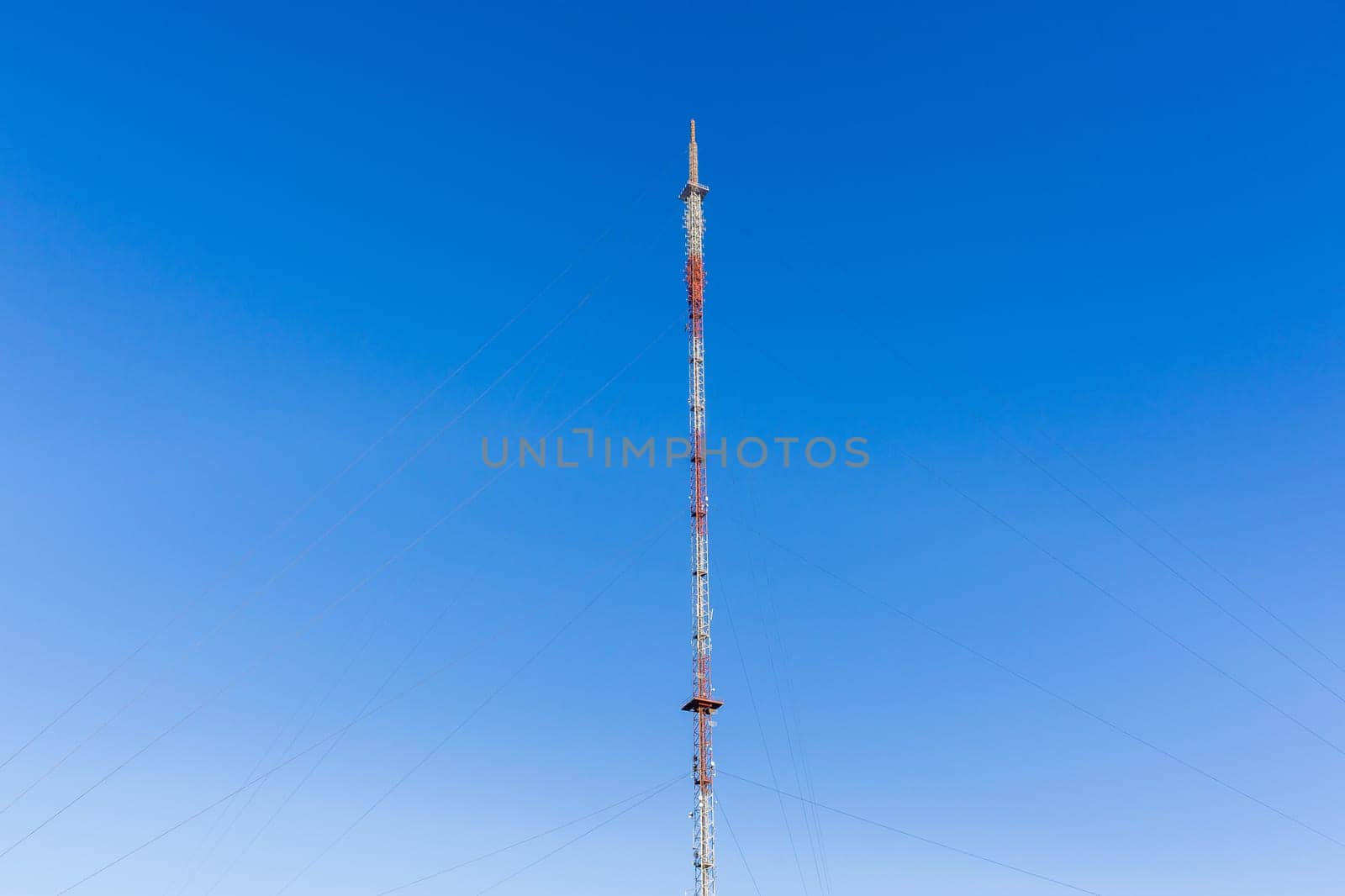 Communications signal tower tall high steel structure,on high ground hilltop for radio tv mobile phones against blue sky.