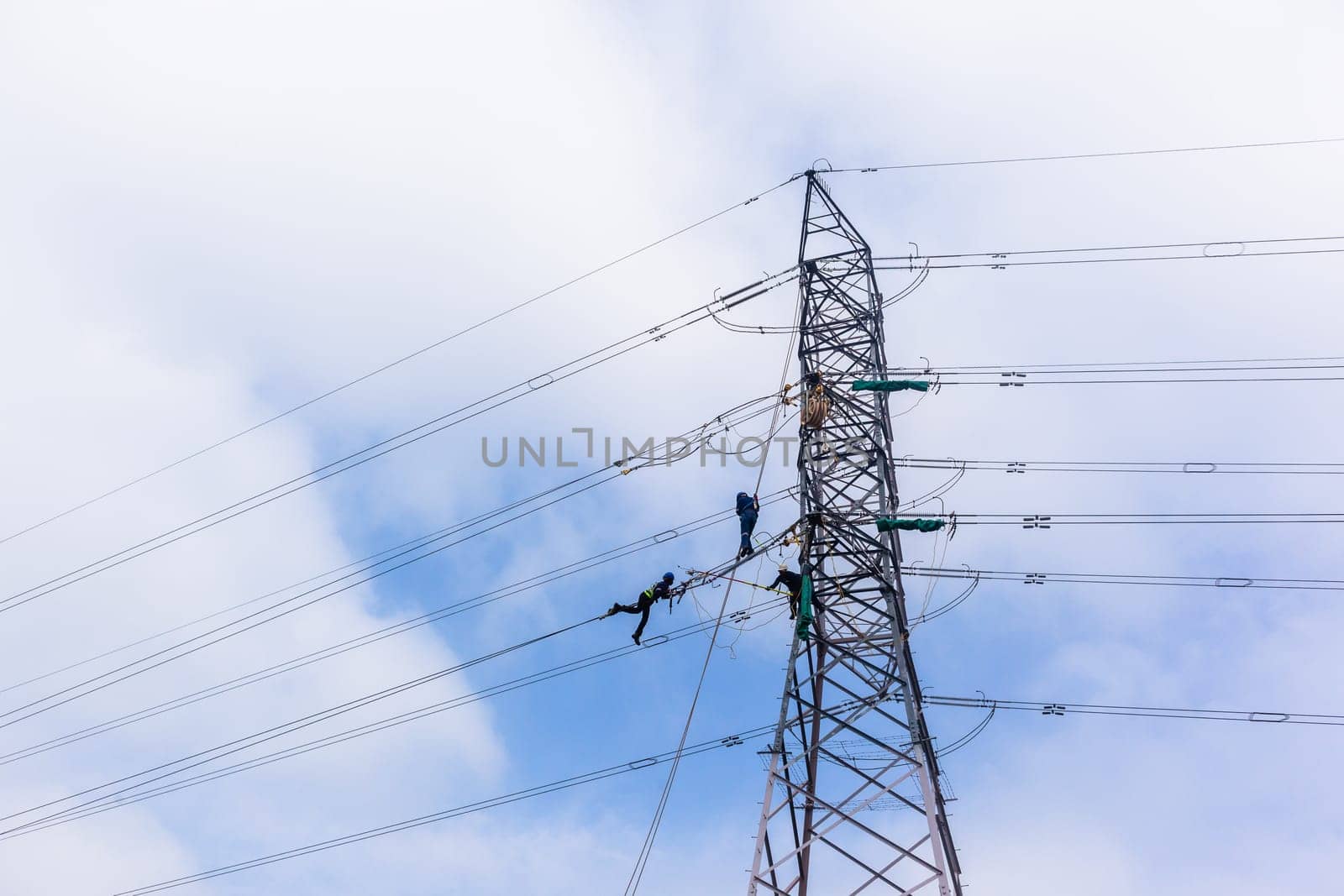 Electricians high rigging working maintnance on electrical cable power lines on steel tower structure.