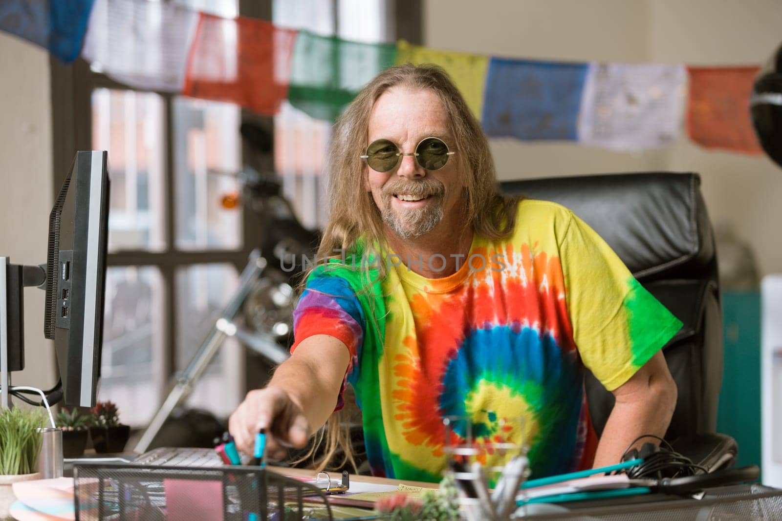 Smiling man in tie dye shirt and round glasses at his desk