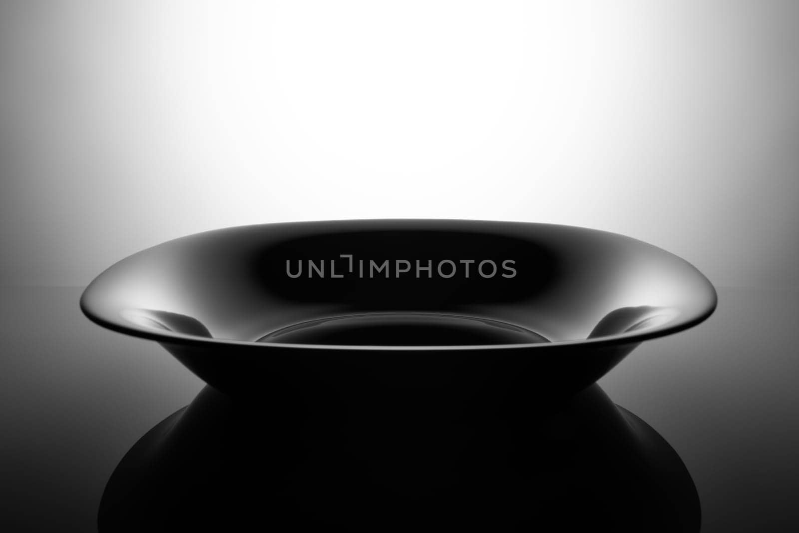 Empty black soup plate, isolated in the shadows.