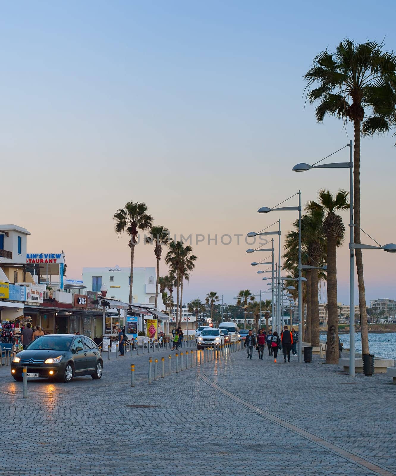 PAPHOS, CYRPUS - FEBRUARY 13, 2019: People walking by Cyprus promenade at twilight. Paphos - famous tourist destination in Cyprus