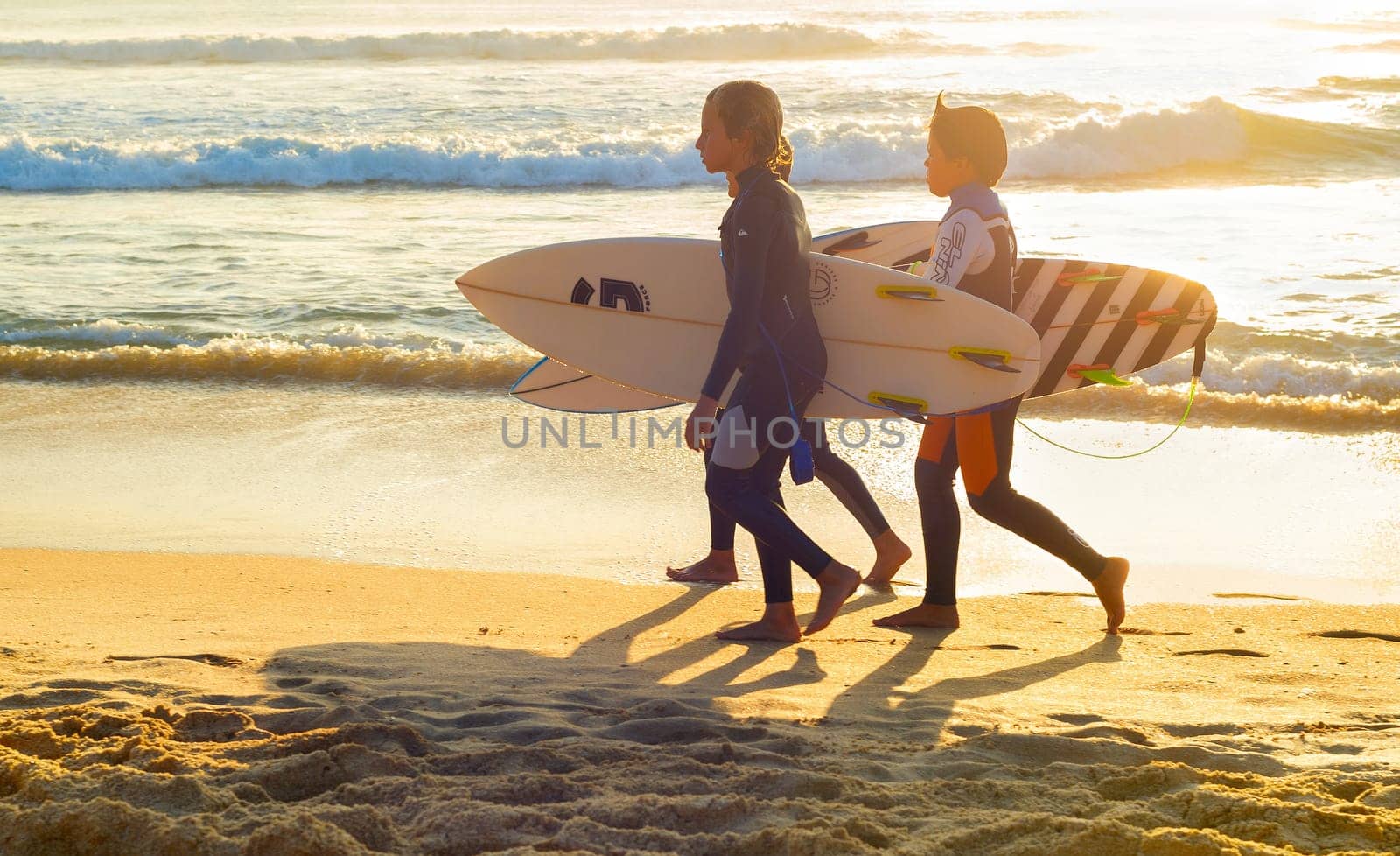 PENICHE, PORTUGAL - OCTOBER 20, 2018: Three boys in wetsuits with surfboards at ocean coast, Peniche, Portugal