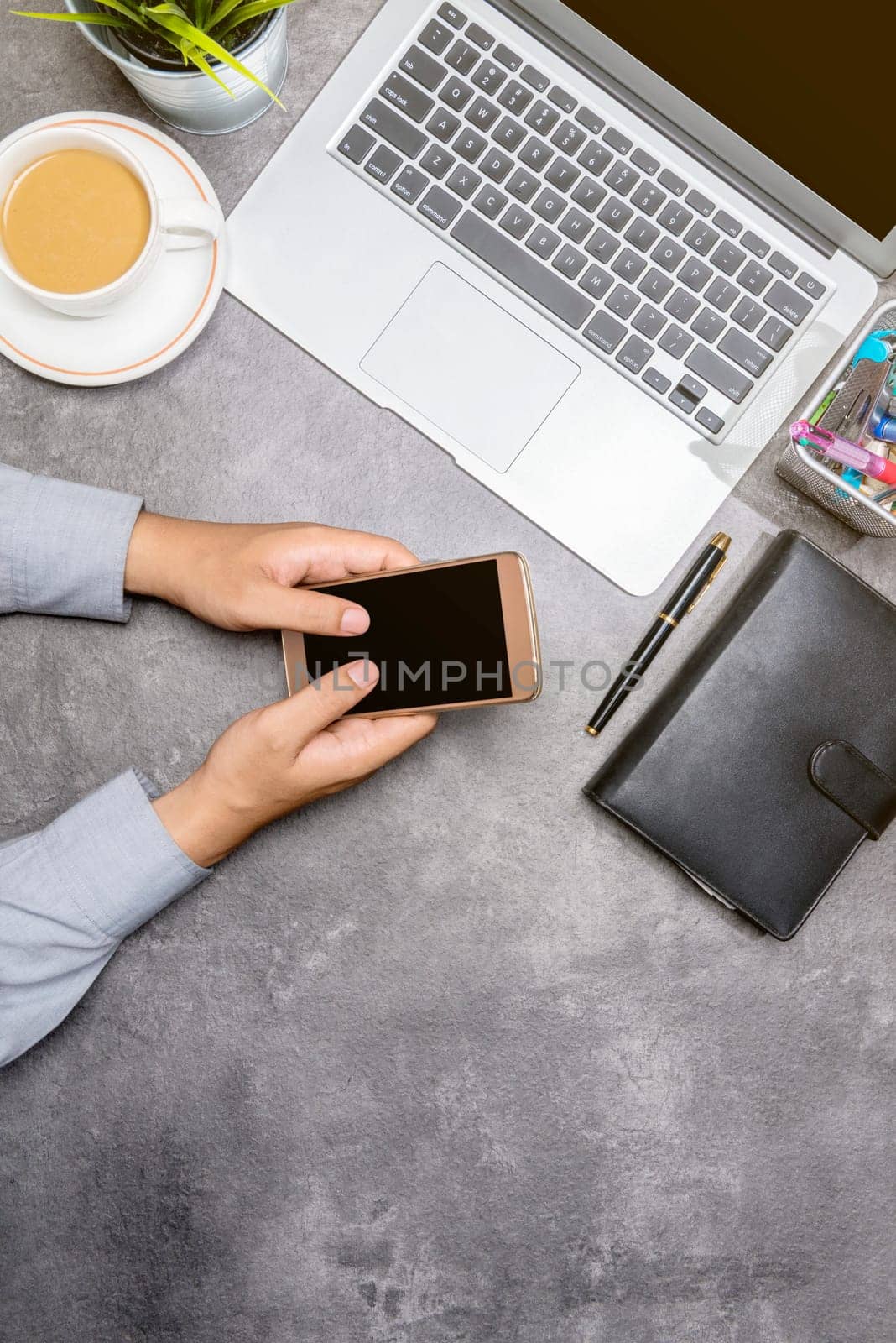 Top view of businessman using mobile phone with laptop, coffee, potted plant, notebook and business accessories on the office desk