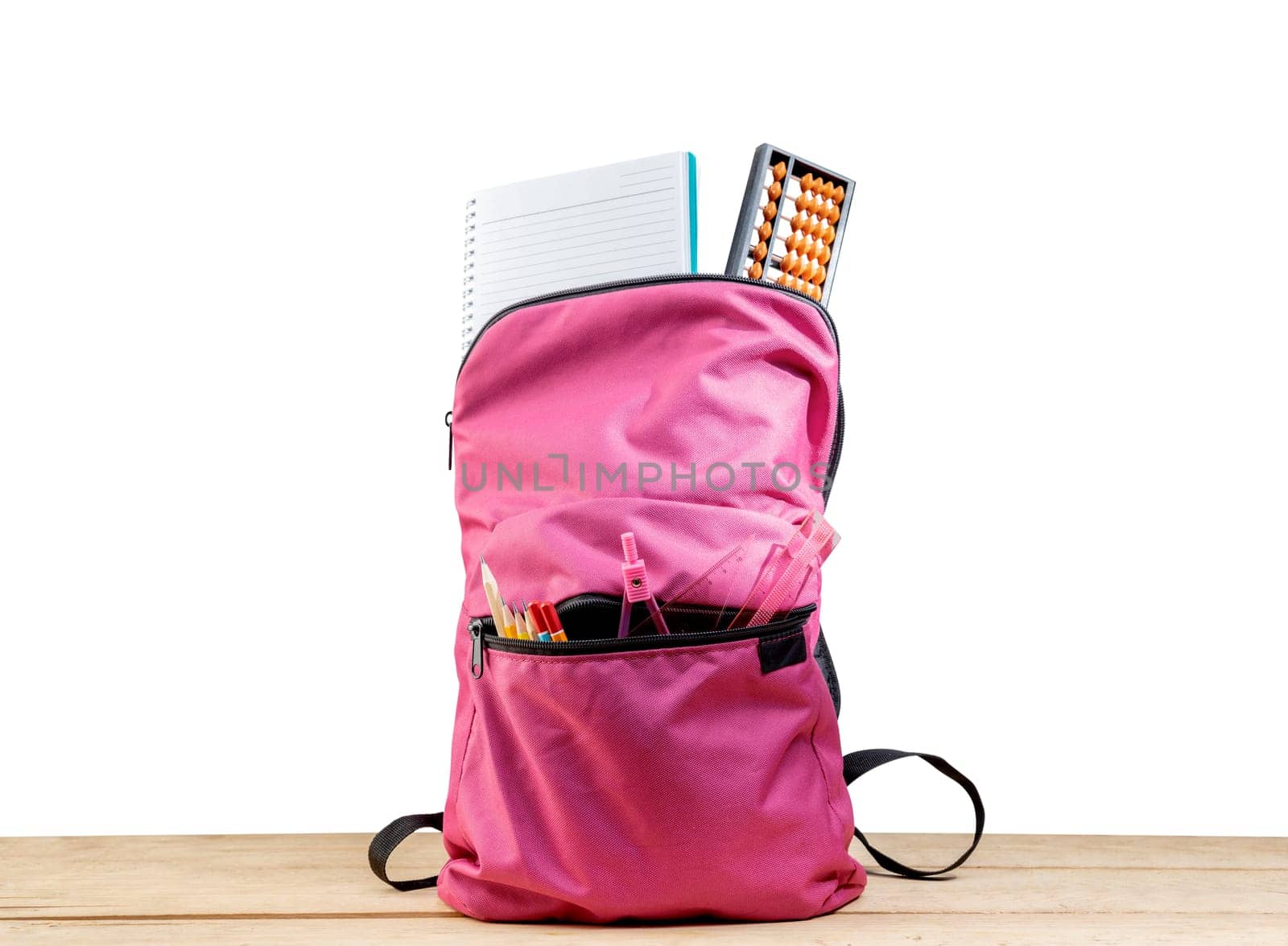 Pink backpack with book and different stationery on wooden table isolated over white background. Back to School concept