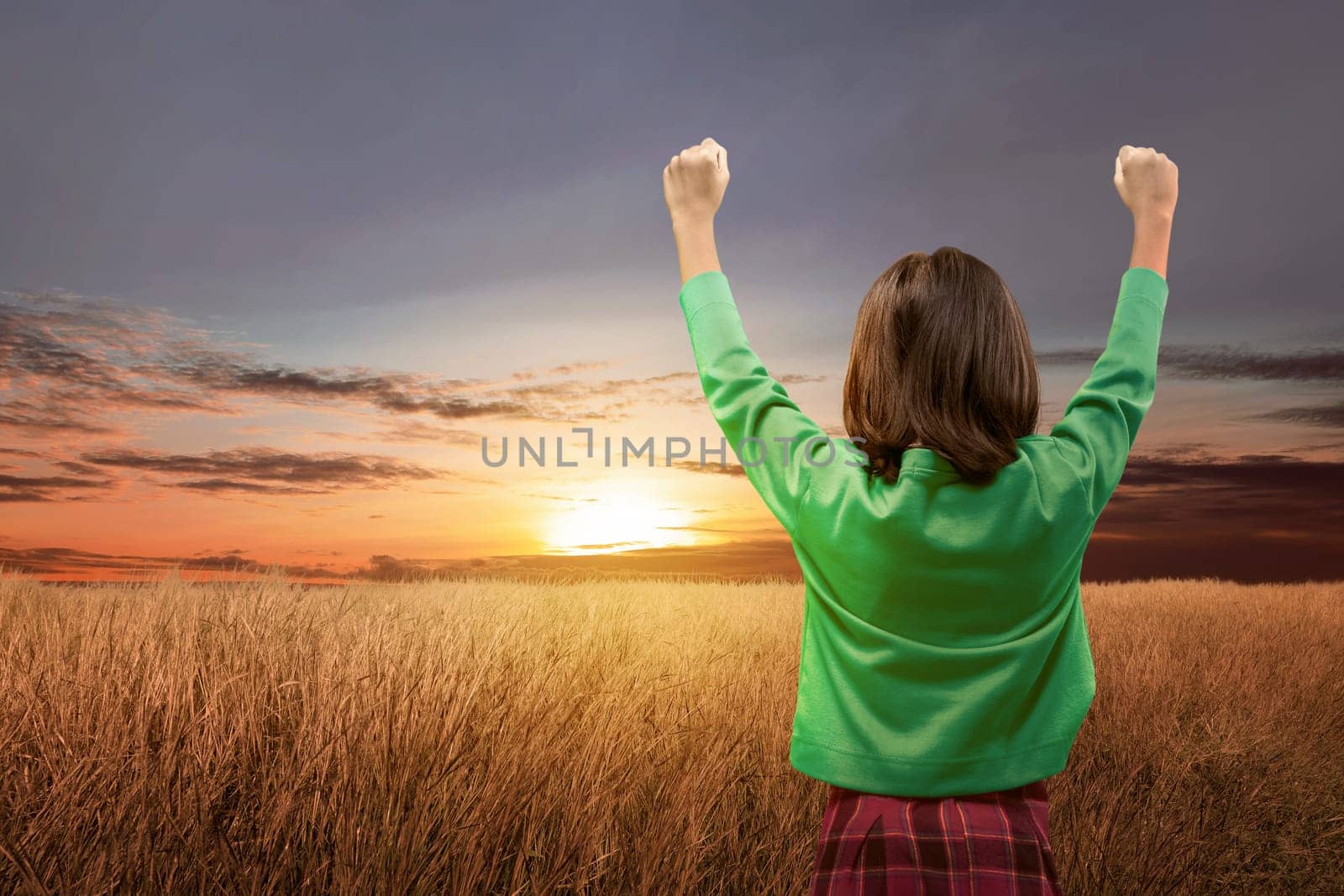 Rear view of asian cute girl standing while raised arms on the meadow field over sunset background. Back to School concept