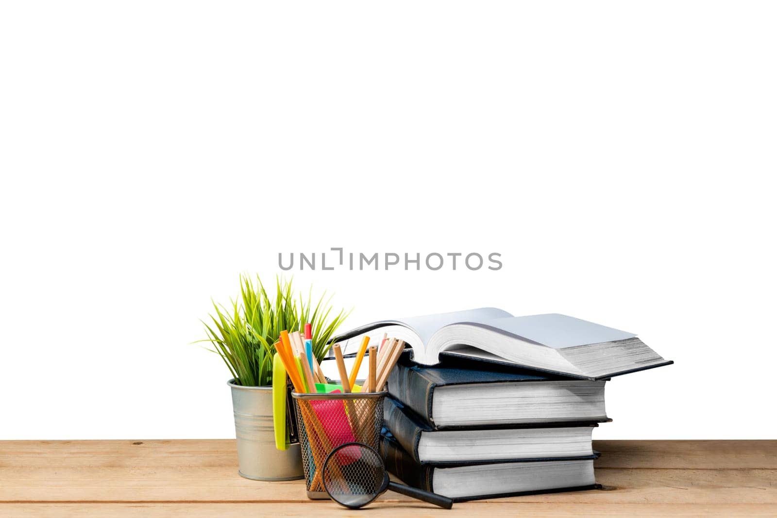 Pile of books with potted plant and pencils in basket container with magnifying glass on wooden table isolated over white background. Back to School concept