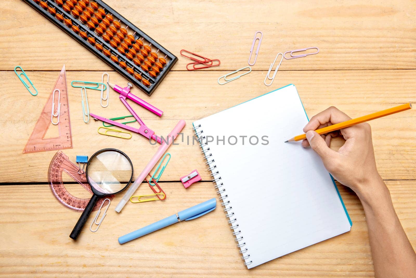 Student writing in notebook with school supplies and stationery on the wooden table. Back to School concept