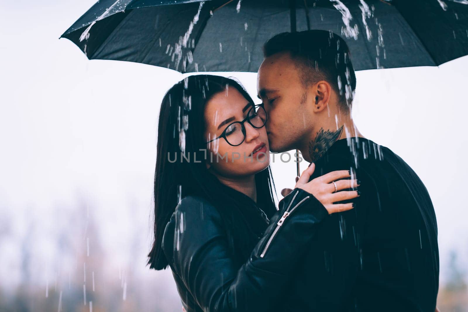 young couple standing under a dark umbrella.