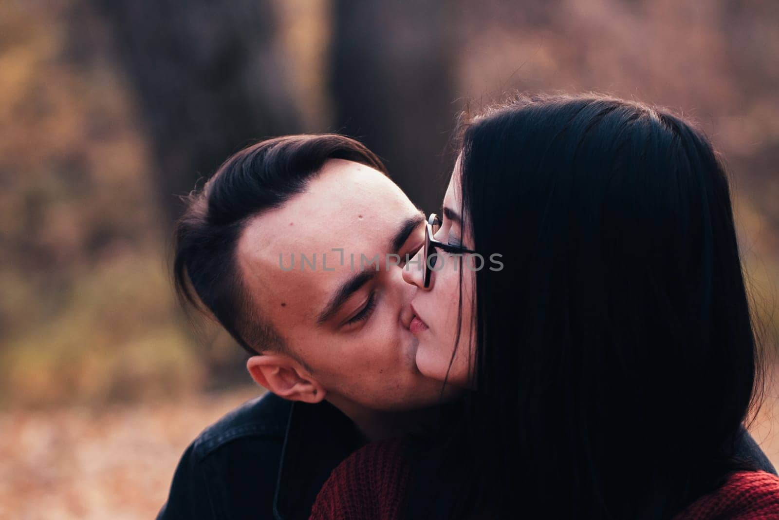 young man and young woman are sitting on a plaid in an autumn forest.