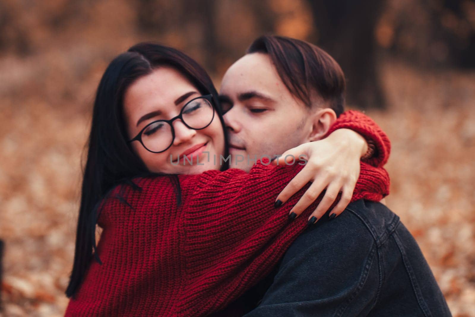 young man and young woman are sitting on a plaid in an autumn forest.