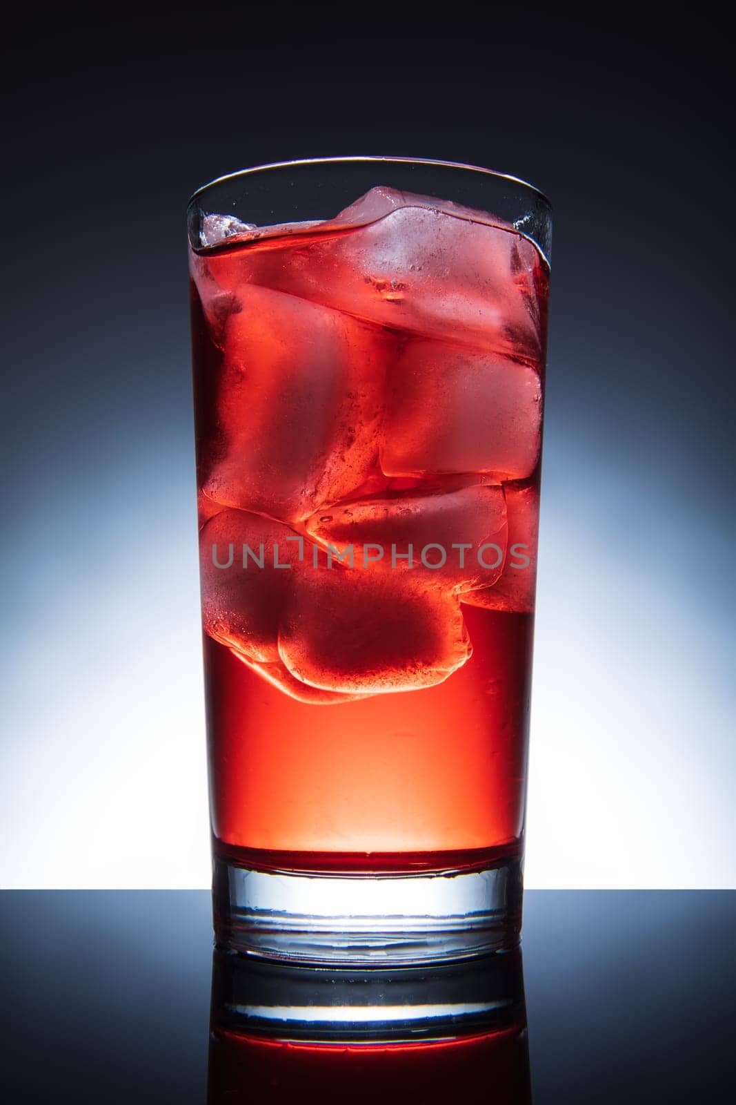 Red cocktail with ice, isolated tall glass.