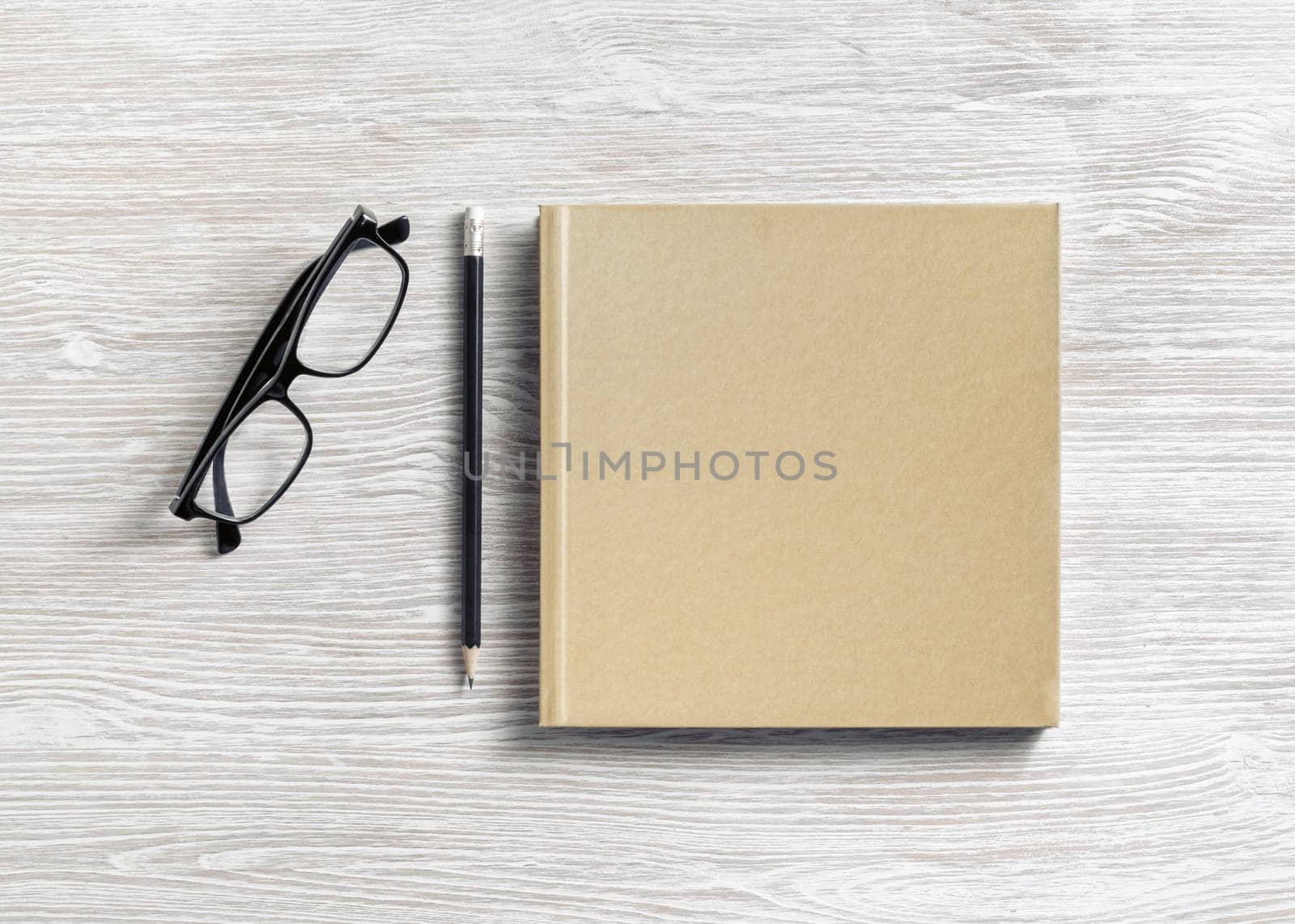 Photo of closed blank square book or notepad, glasses and pencil on wooden background. Template for placing your design. Flat lay.