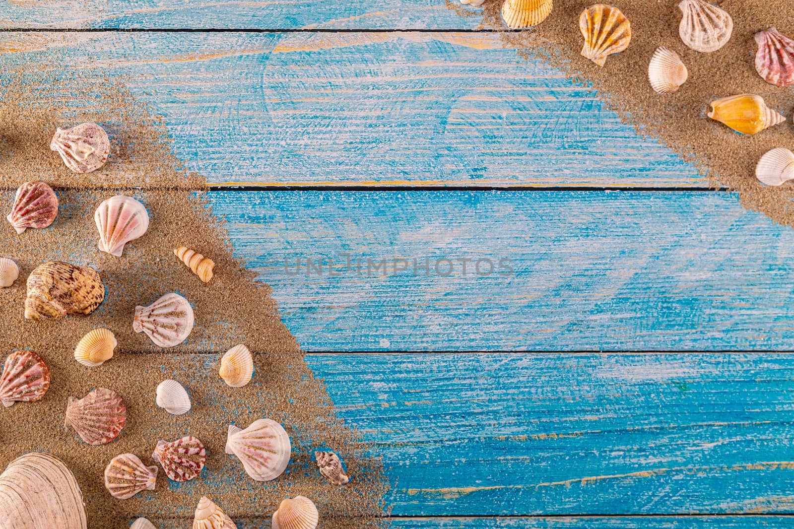 Summer time concept with sea shells on a blue wooden background and sand. Seashells frame on wooden background nautical border. Focus on seashells.