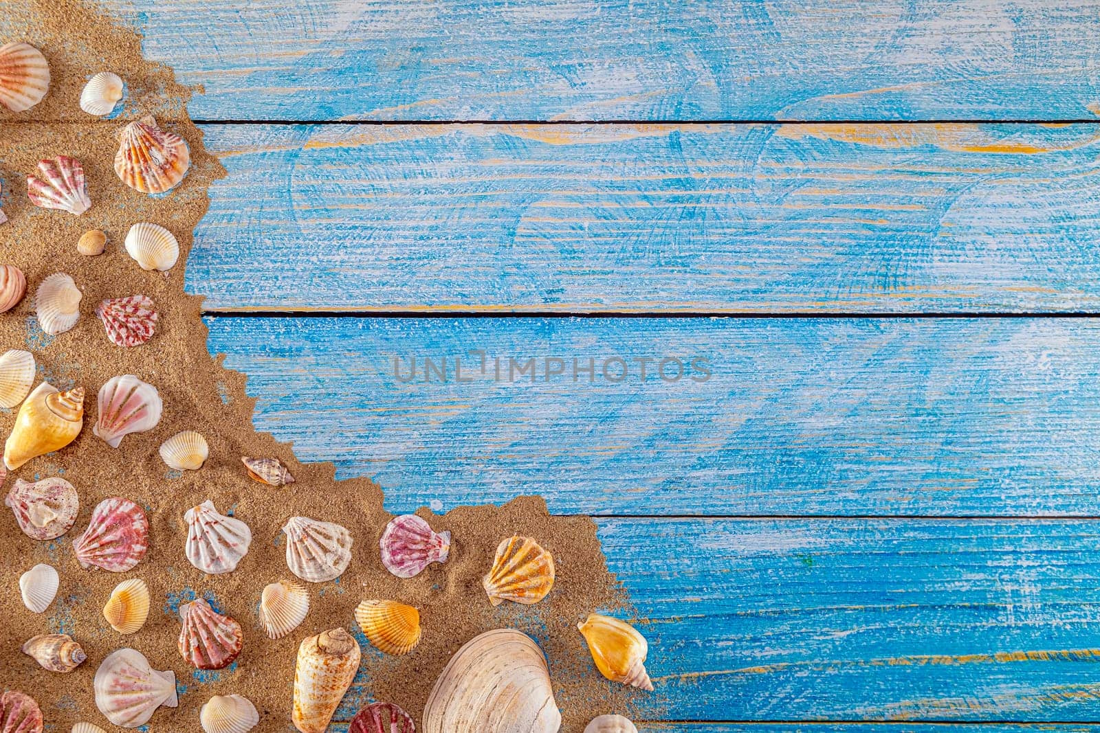 Summer time concept with sea shells on a blue wooden background and sand. Seashells frame on wooden background nautical border. Focus on seashells.