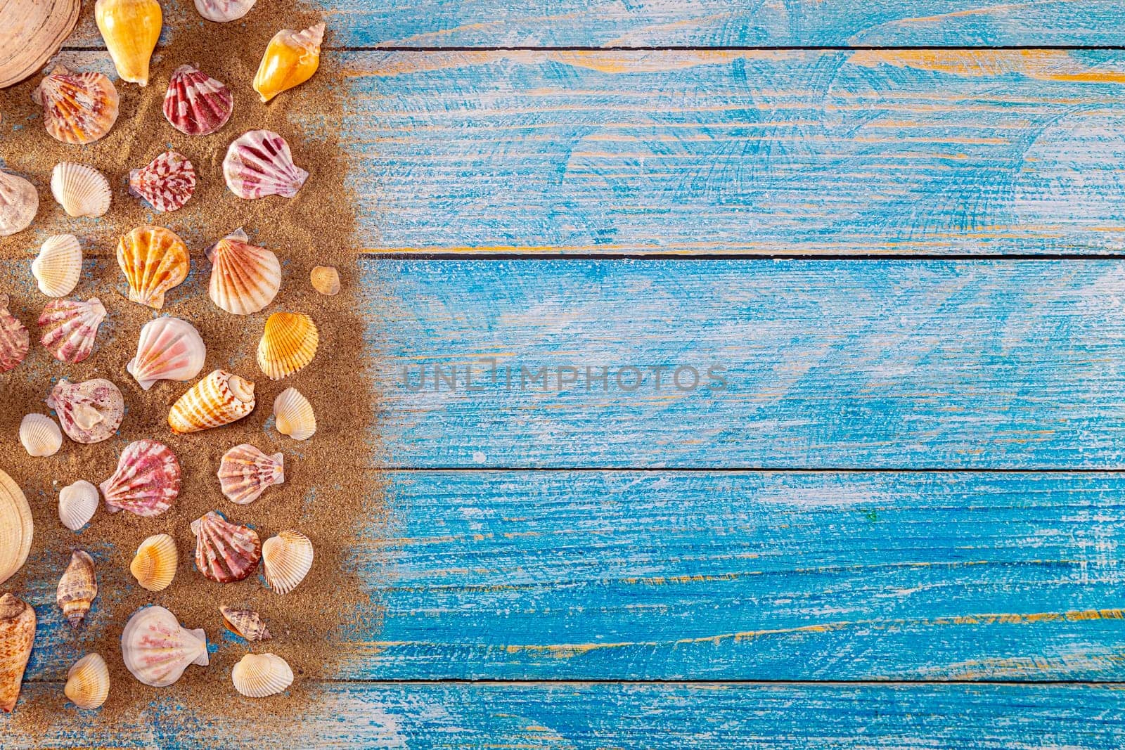 Summer time concept with sea shells on a blue wooden background and sand. Seashells frame on wooden background nautical border. Focus on seashells.